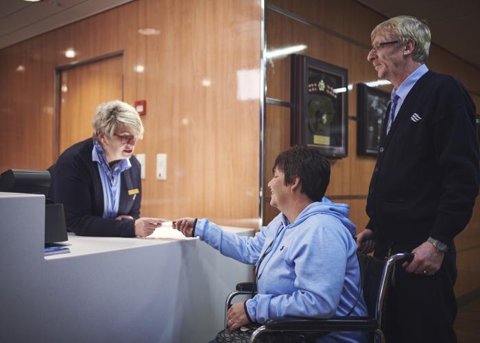 woman at desk handing card over to woman in wheelchair