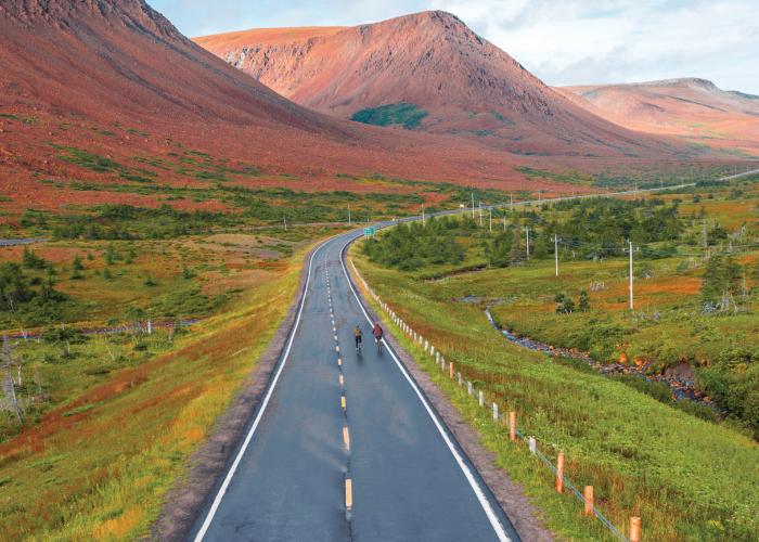 two bikers on empty road with mountains in background